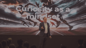 Actionable Futurist Andrew Grill on stage in front of an image that says "Curiosity as a Mindset"
